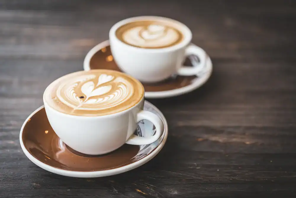 Two cups of coffee with heart-shaped latte art sit on brown saucers atop a dark wooden table, capturing the cozy vibe of a charming cafe NYC locals love.