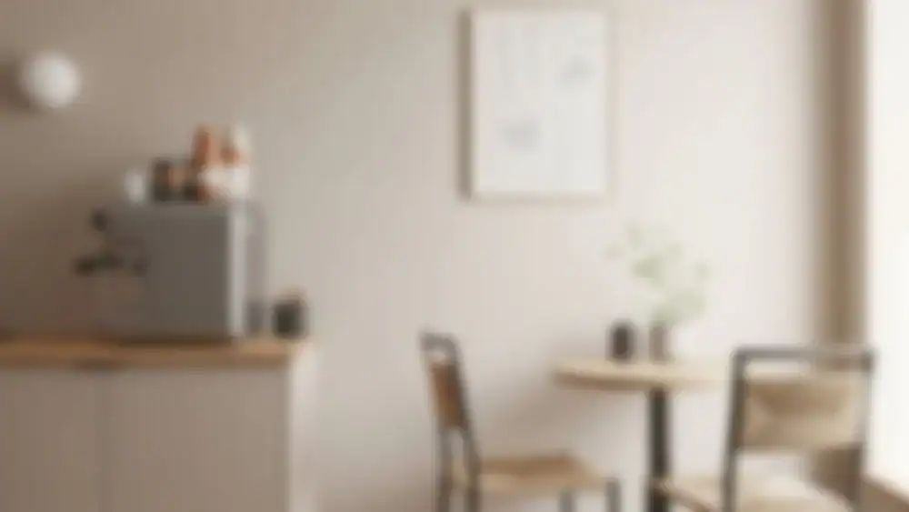 A blurred image of a small, cozy kitchen or dining area evokes the charm of an Art Gallery Cafe in NYC, featuring a table, two chairs, a coffee machine on the counter, and a framed picture on the wall.