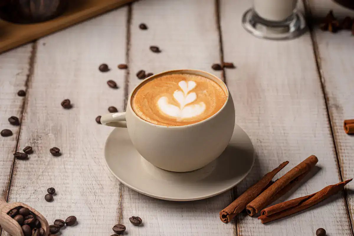 A cup of coffee with latte art on top sits on a saucer on a white wooden table at the Art Gallery Cafe in NYC