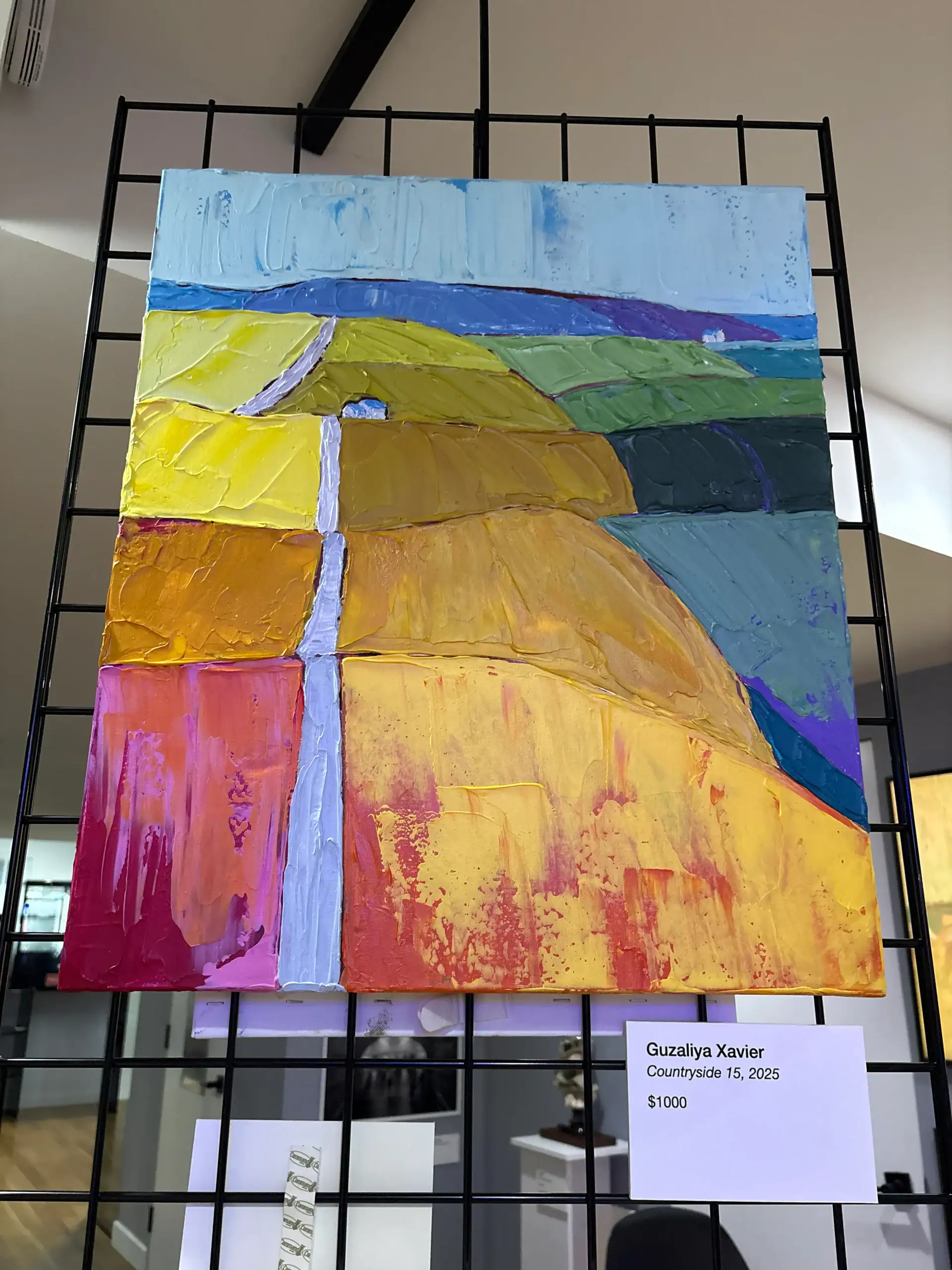 A colorful abstract landscape painting displayed on a black metal grid in a chic NYC wine bar and art gallery.