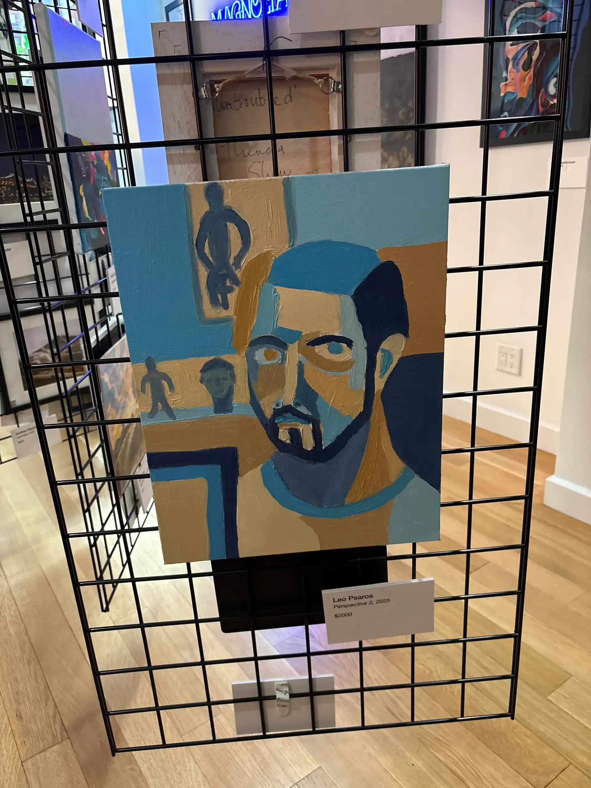 An abstract colorful portrait of a man hangs on a wire grid at a Wine Bar & Art Gallery in NYC.