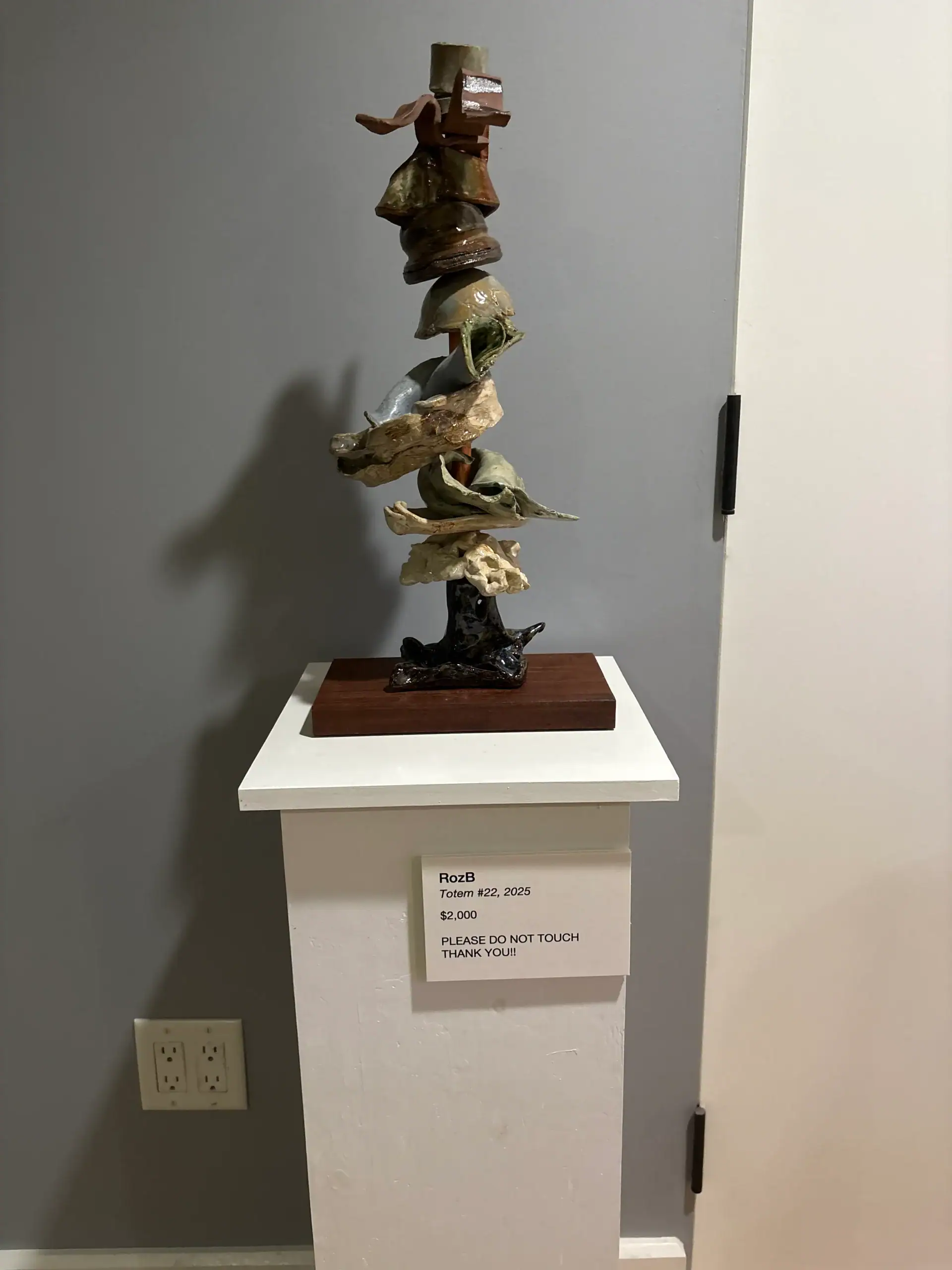 Abstract sculpture of stacked shapes on a pedestal at NYC Wine Bar & Art Gallery with a “do not touch” sign.