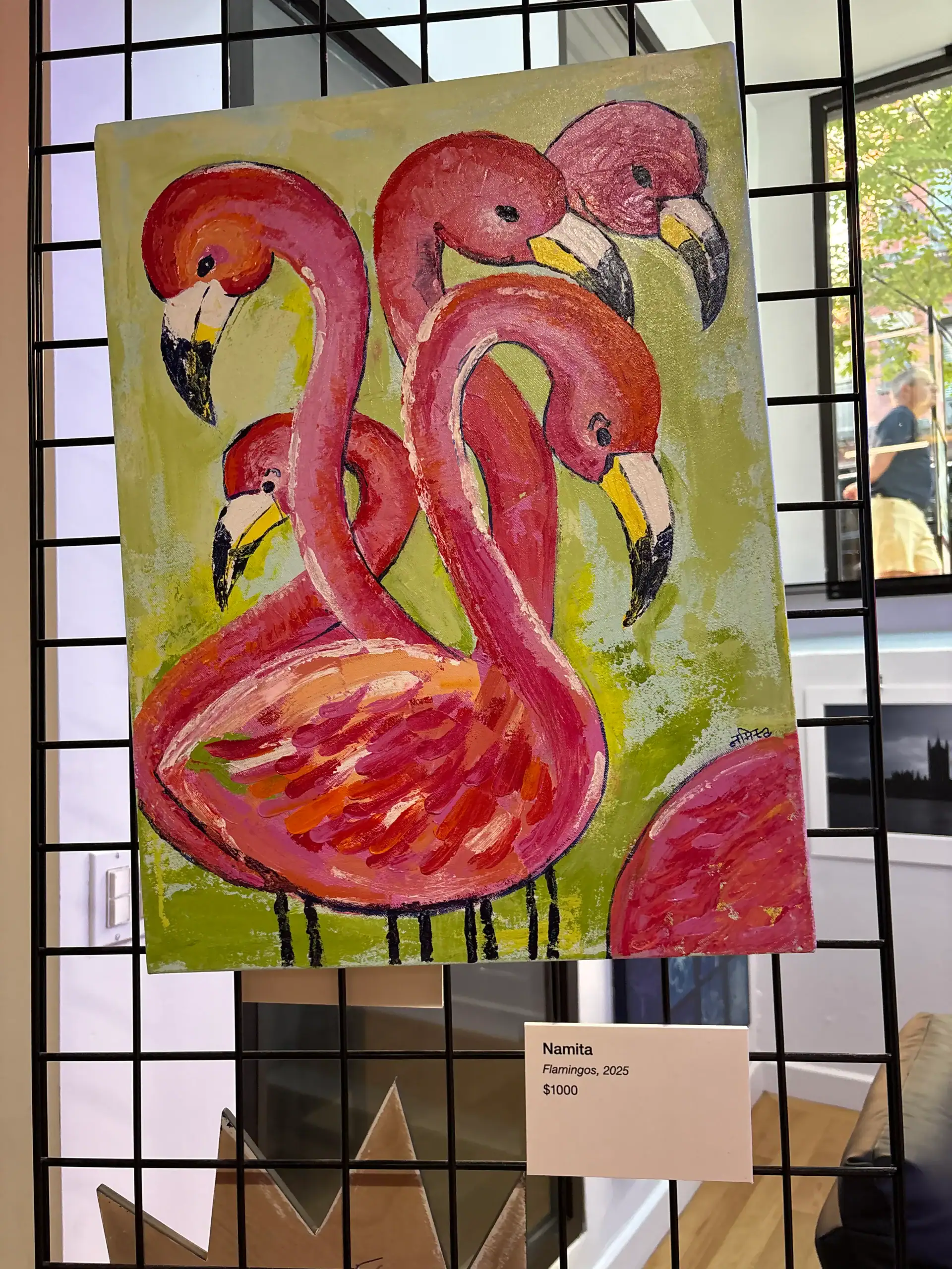A vibrant painting of five pink flamingos on green hangs in a Wine Bar & Art Gallery in NYC.