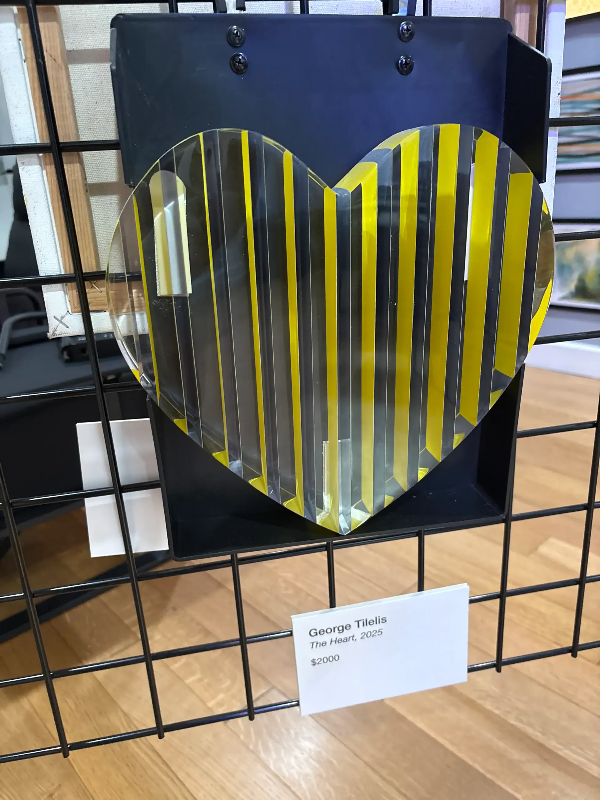 Yellow and clear striped heart-shaped artwork displayed on a metal grid at a NYC Wine Bar & Art Gallery.